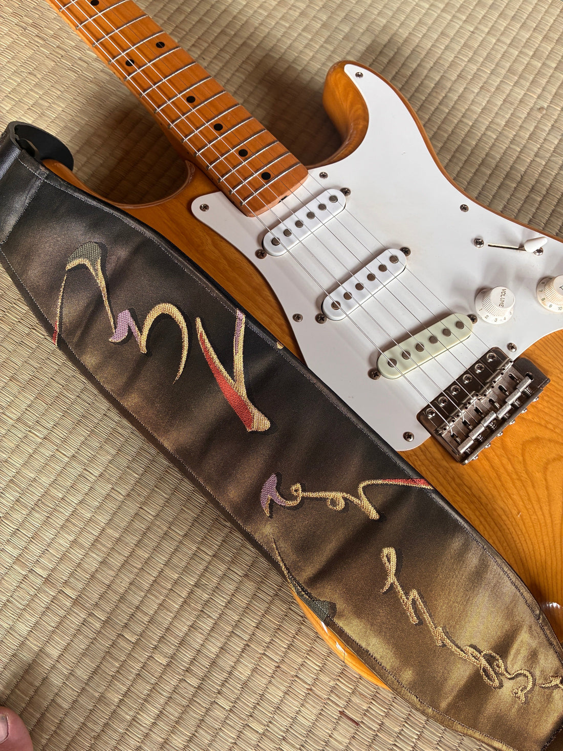 OGF wide guitar strap with a dark woven pattern laid across a natural-finish electric guitar on tatami.